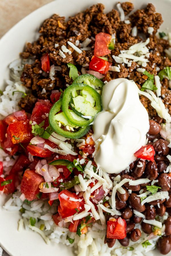 a white plate topped with rice, beans and vegetables next to sour cream on top