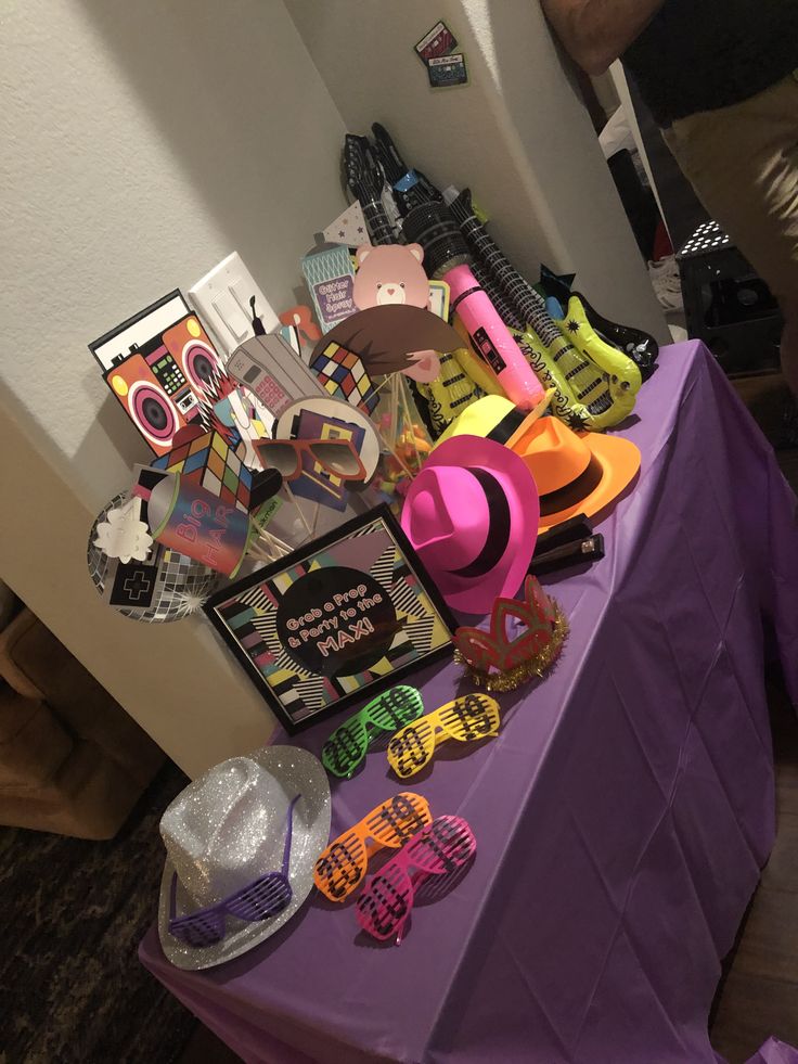 a purple table topped with lots of hats and other items next to a white wall