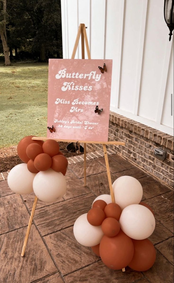 a sign with balloons in the shape of butterflies on it and an easel holding a sign that says butterfly kisses