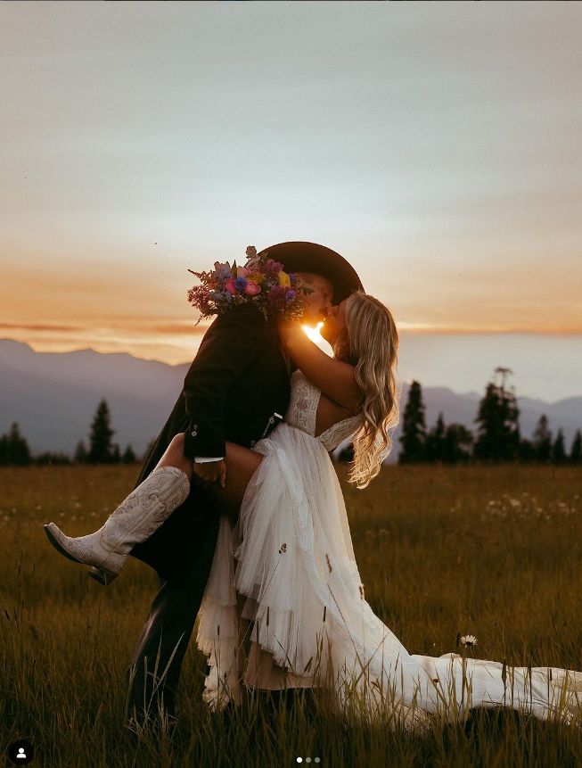 a bride and groom kissing in a field at sunset