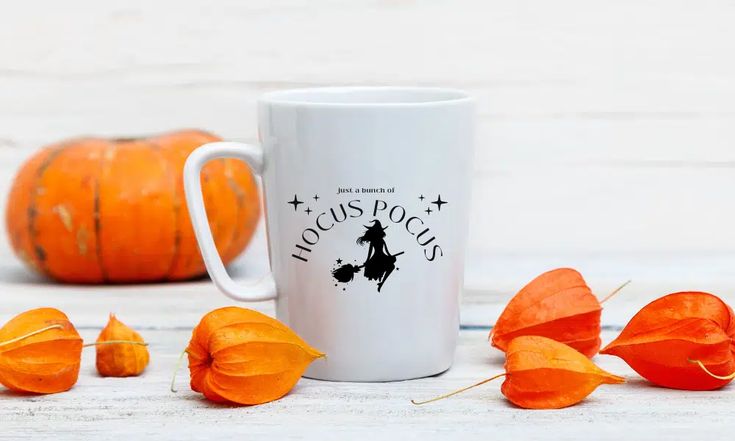 a white coffee mug sitting on top of a wooden table next to orange pumpkins