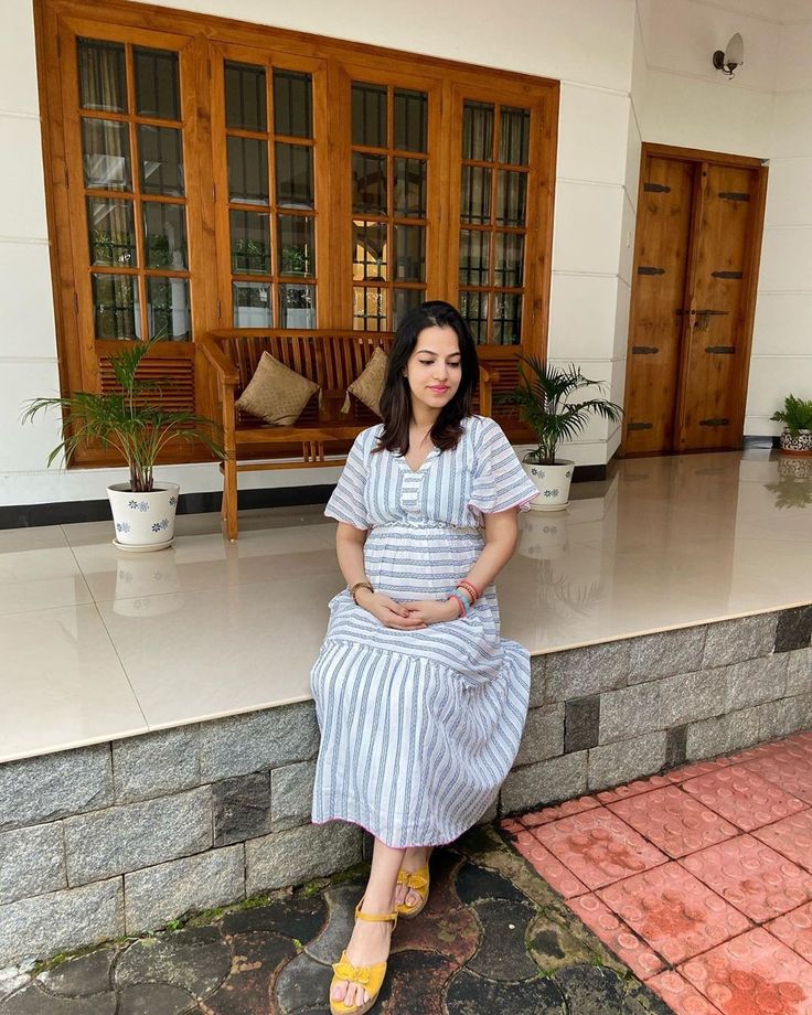 a pregnant woman sitting on the ground in front of a building with wooden doors and windows