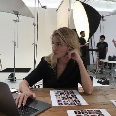 a woman sitting at a table with a laptop in front of her and people behind her