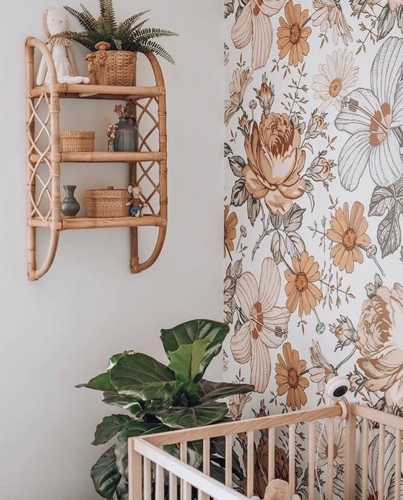 a baby crib next to a wall with flowers on it and a potted plant in the corner