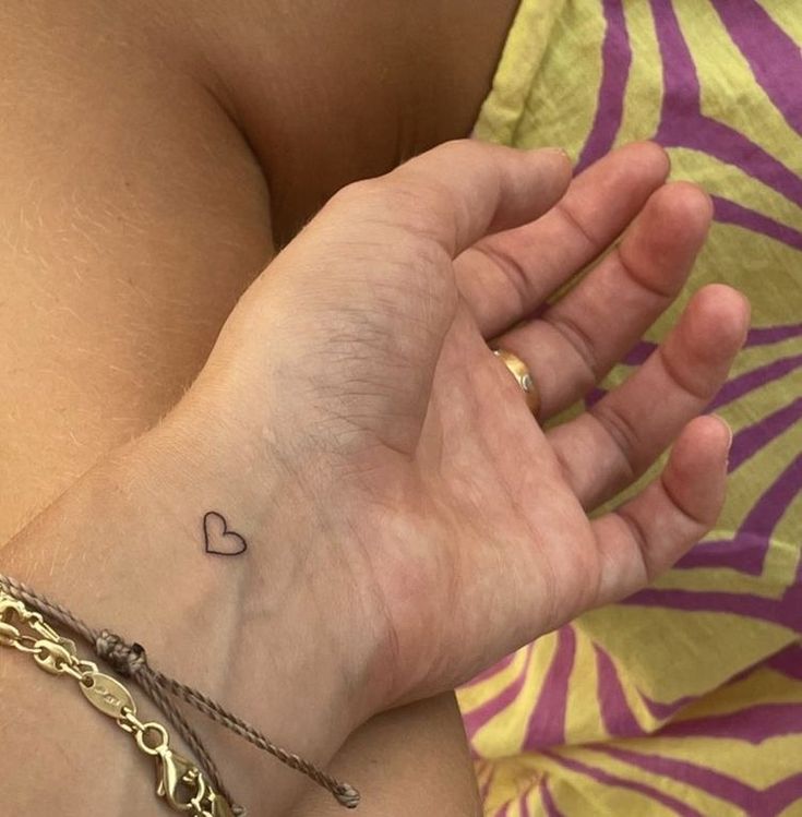 a woman's arm with a small heart tattoo on her left wrist and gold chain bracelet