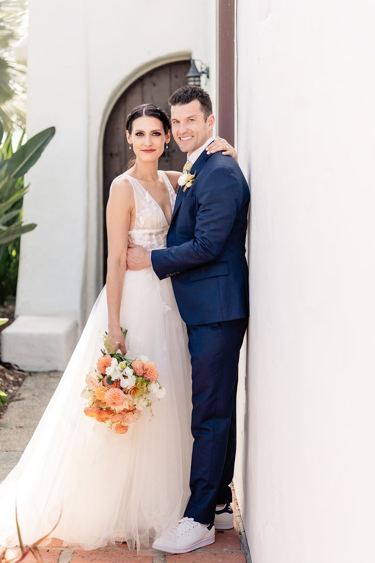 a bride and groom standing next to each other in front of a white stucco wall