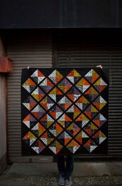 a person holding up a quilt in front of a garage door