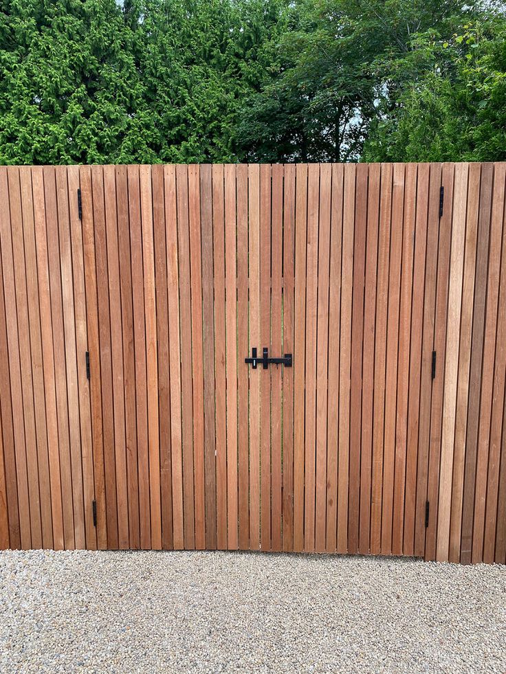 a wooden fence with two black knobs on it's sides and trees in the background