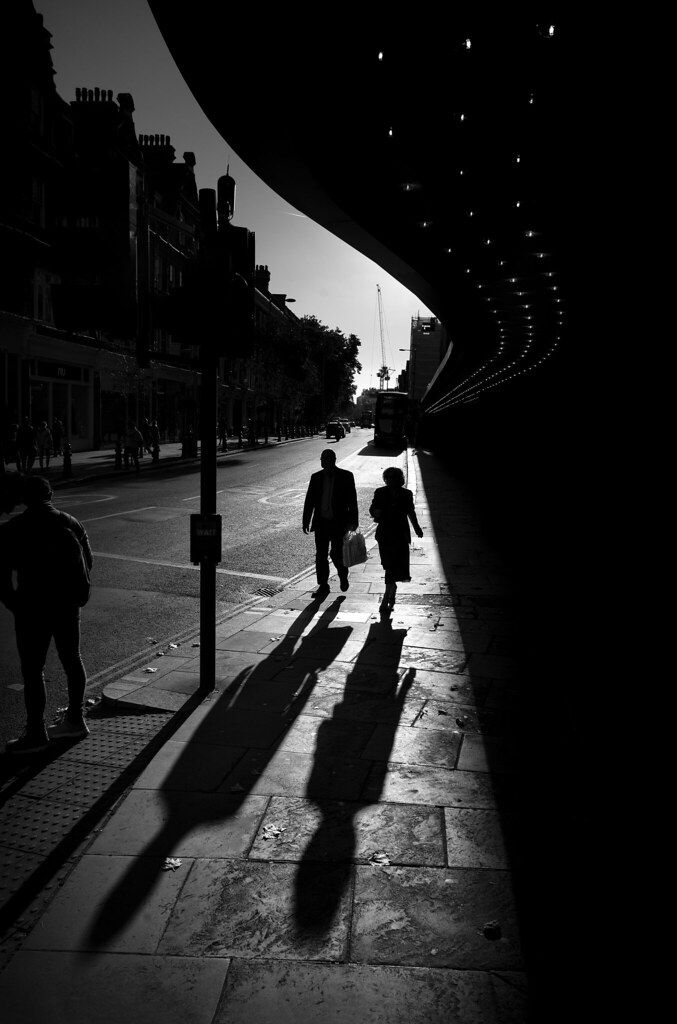 black and white photograph of people walking down the street with their shadows on the ground