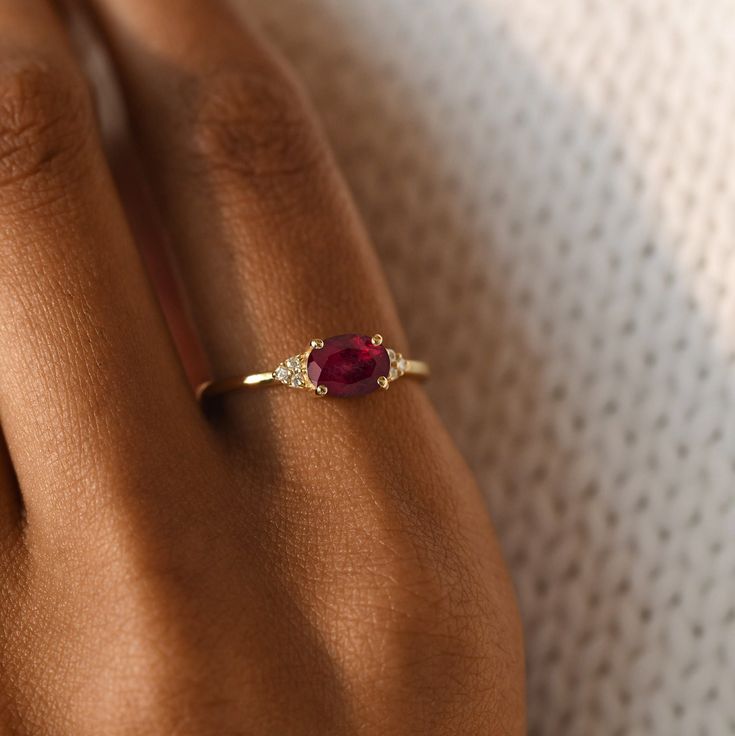 a woman's hand wearing a gold ring with a ruby stone and diamond accents