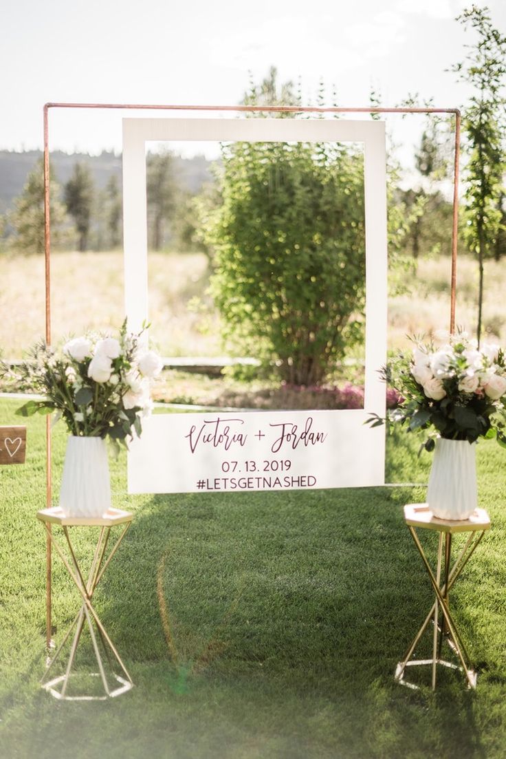 an outdoor ceremony setup with white flowers in vases and gold stand on the grass