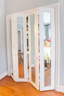 an empty room with mirrored doors and hardwood flooring in the corner, looking into another room