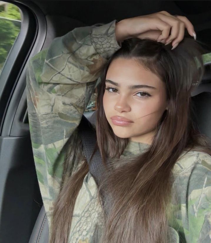 a woman sitting in the back seat of a car with her hair pulled up and wearing an army uniform