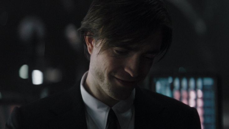 a man wearing a suit and tie looking at his cell phone in a dark room