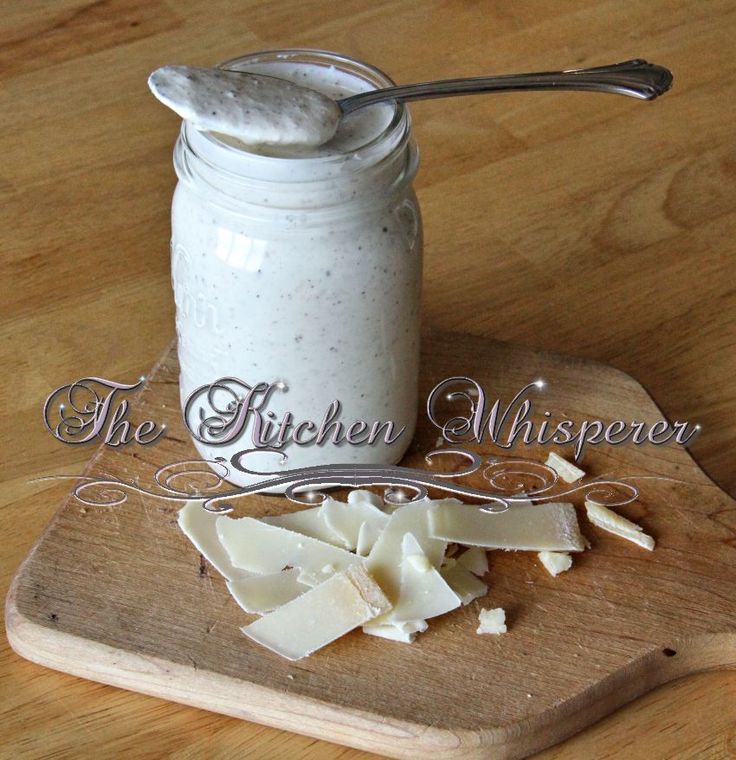 a wooden cutting board topped with cheese next to a glass jar filled with white liquid