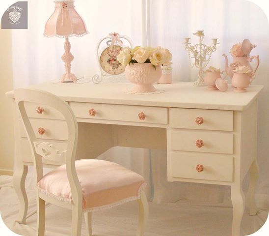 a white desk topped with a pink chair next to a lamp and vase filled with flowers