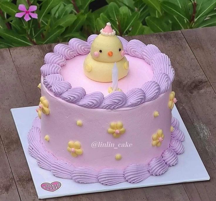 a pink cake with a yellow rubber duck on top and purple icing around the edges