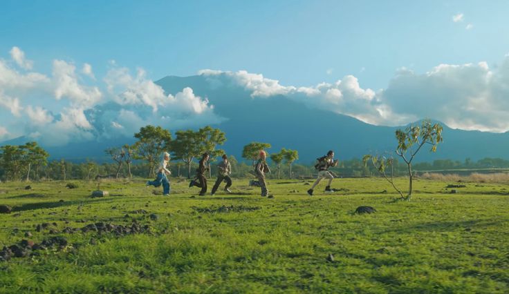 group of people walking across a lush green field with mountains in the background on a sunny day