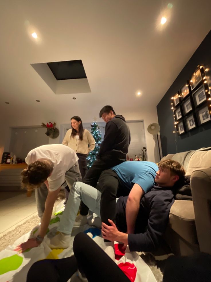 several people in a living room with christmas decorations on the floor and one person laying down