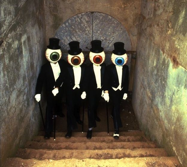 four men in black suits and top hats with eyeballs on their faces are standing at the bottom of some stairs