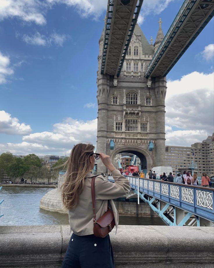 a woman is taking a photo in front of the tower bridge