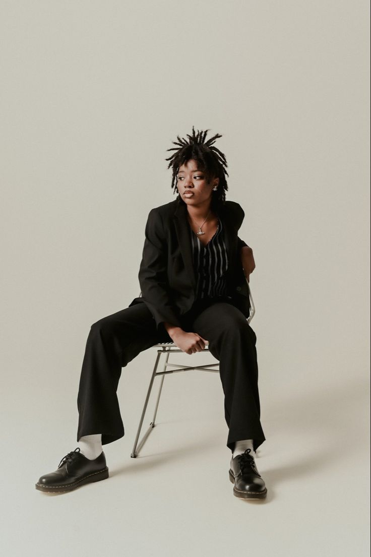 a woman sitting on top of a chair wearing a black suit and white shirt with dreadlocks