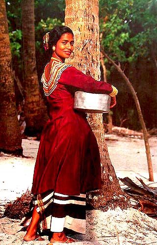 a woman standing next to a tree with a bucket on her head and wearing a red dress