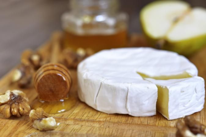 a piece of cheese sitting on top of a wooden cutting board next to an apple