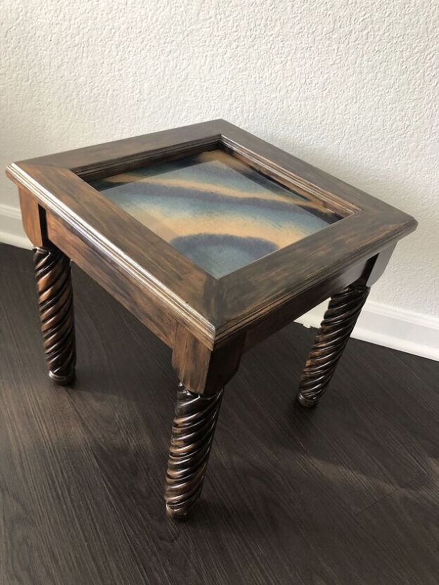 a small wooden table with a painting on it's top and metal spiral legs