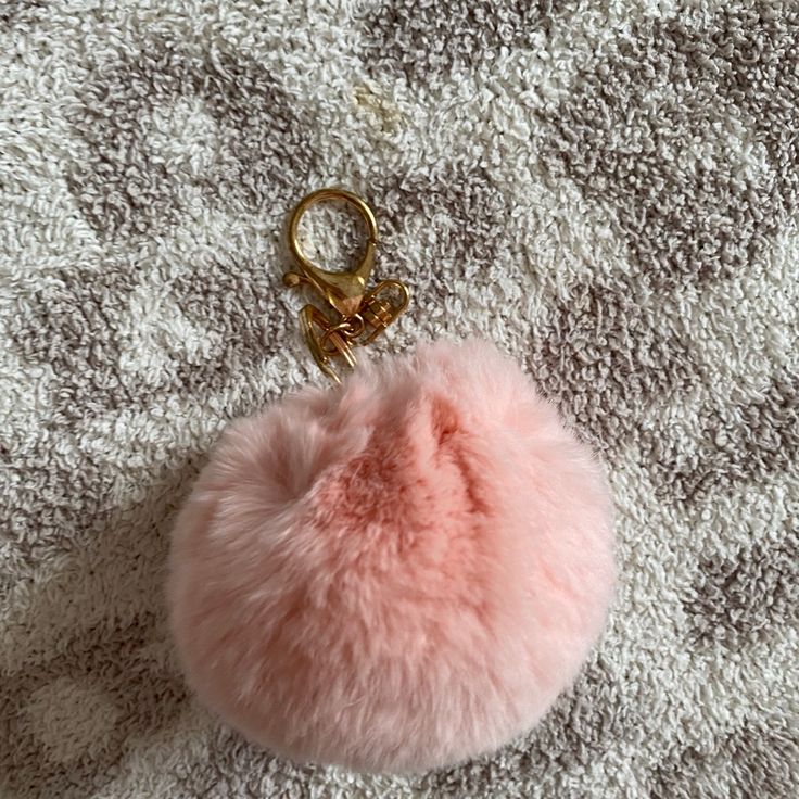 a pink pom - pom keychain laying on top of a white blanket