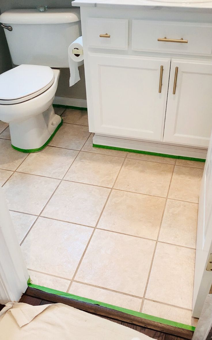 a white toilet sitting in a bathroom next to a sink and shower stall with green tape on the floor