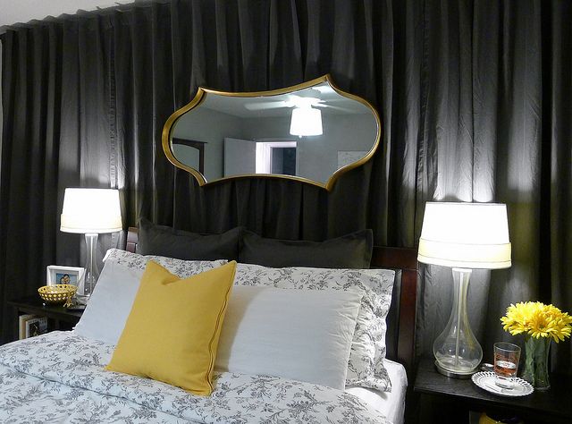 a bedroom with black drapes and white bedding, yellow pillows, and a large mirror on the wall