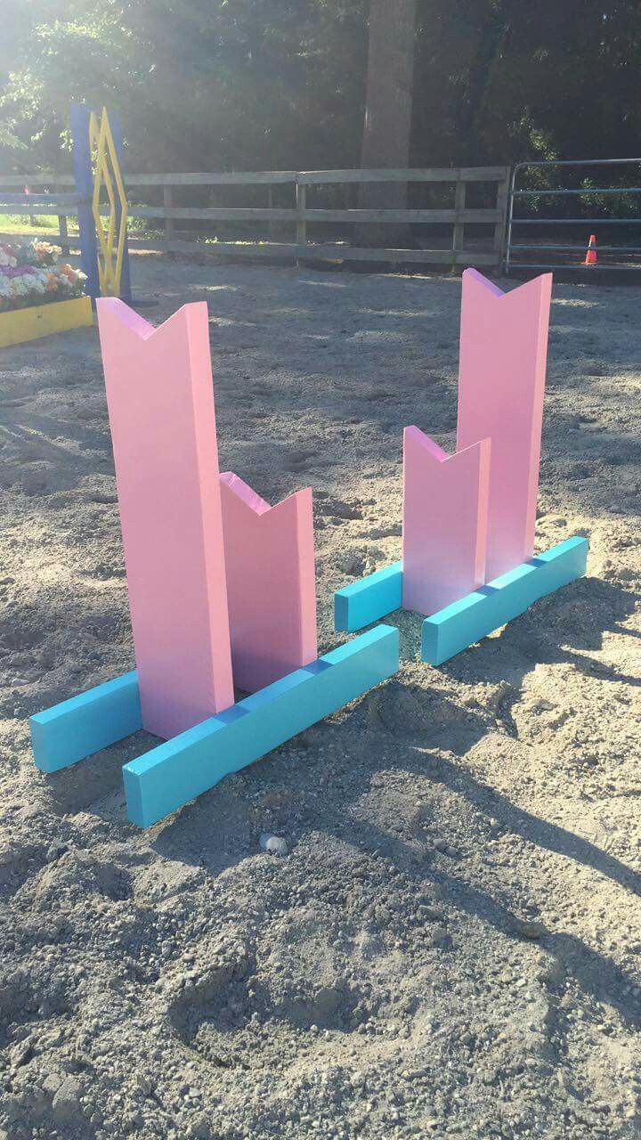 two pink and blue sculptures in the sand at a playground area, with trees in the background