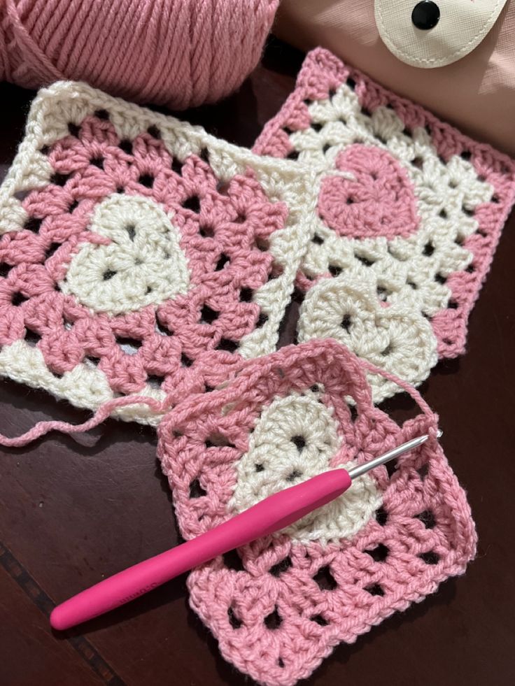 two crocheted squares are next to a pink ball of yarn