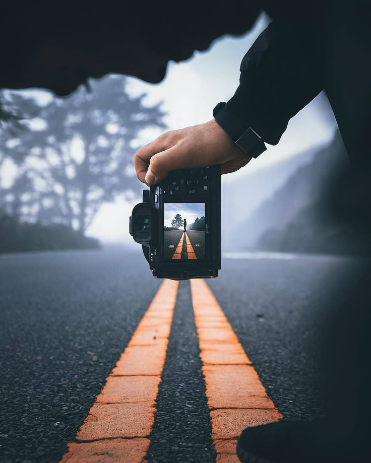 a person holding a camera up to take a photo on an empty road with trees in the background