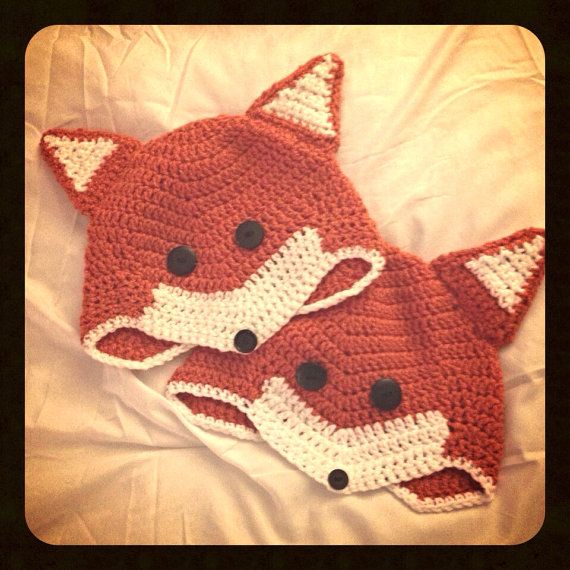 two crocheted fox hats laying on top of a bed