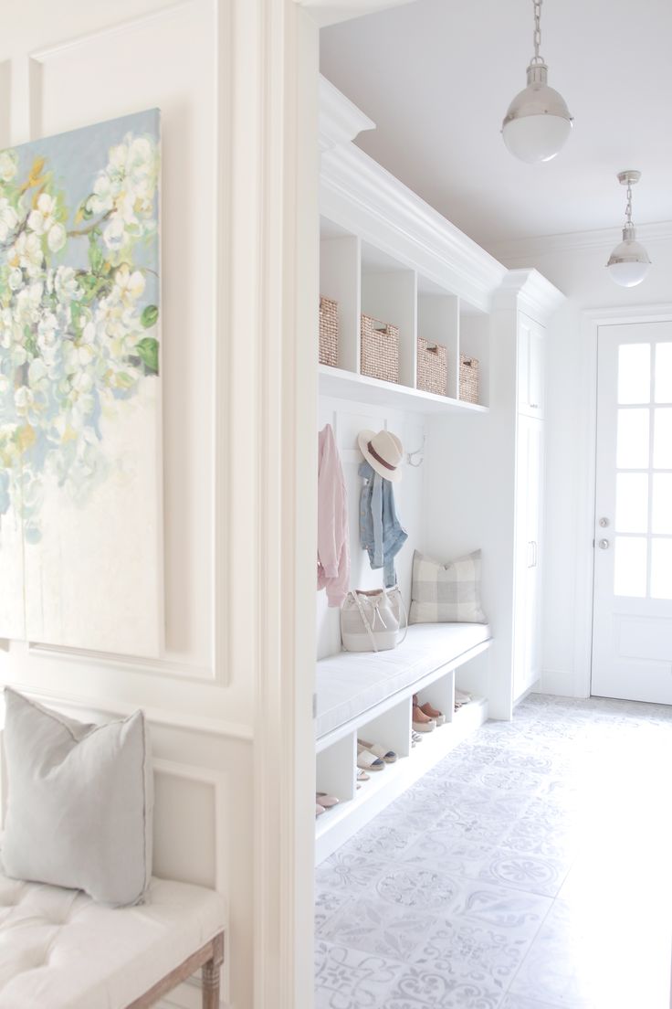 a white entryway with a bench, coat rack and paintings hanging on the wall