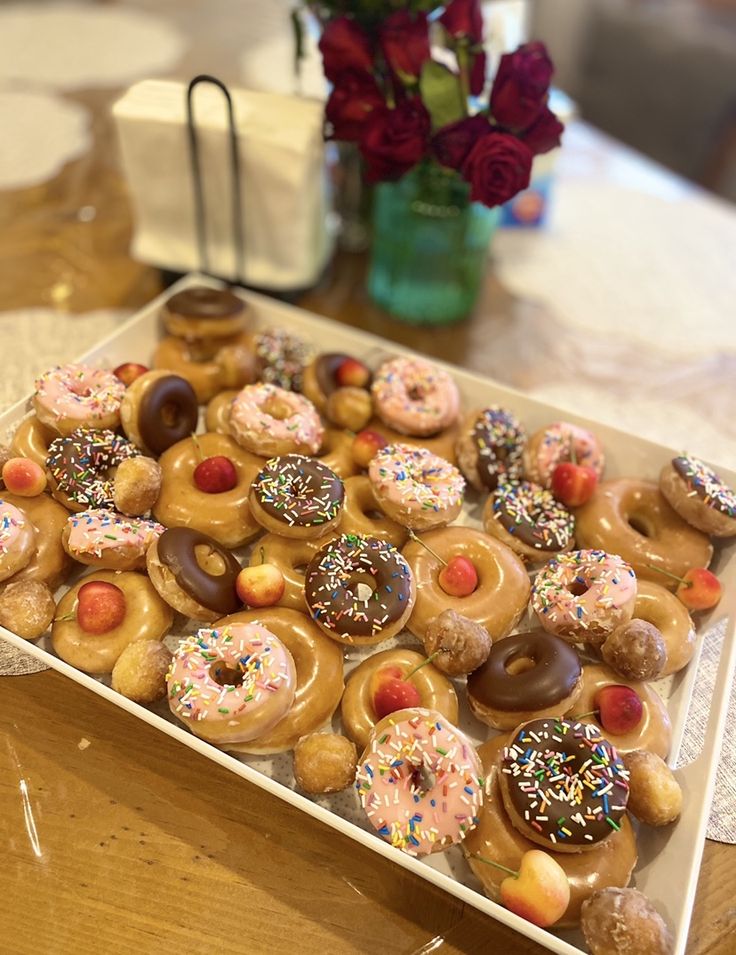 a tray filled with lots of donuts on top of a table next to a vase