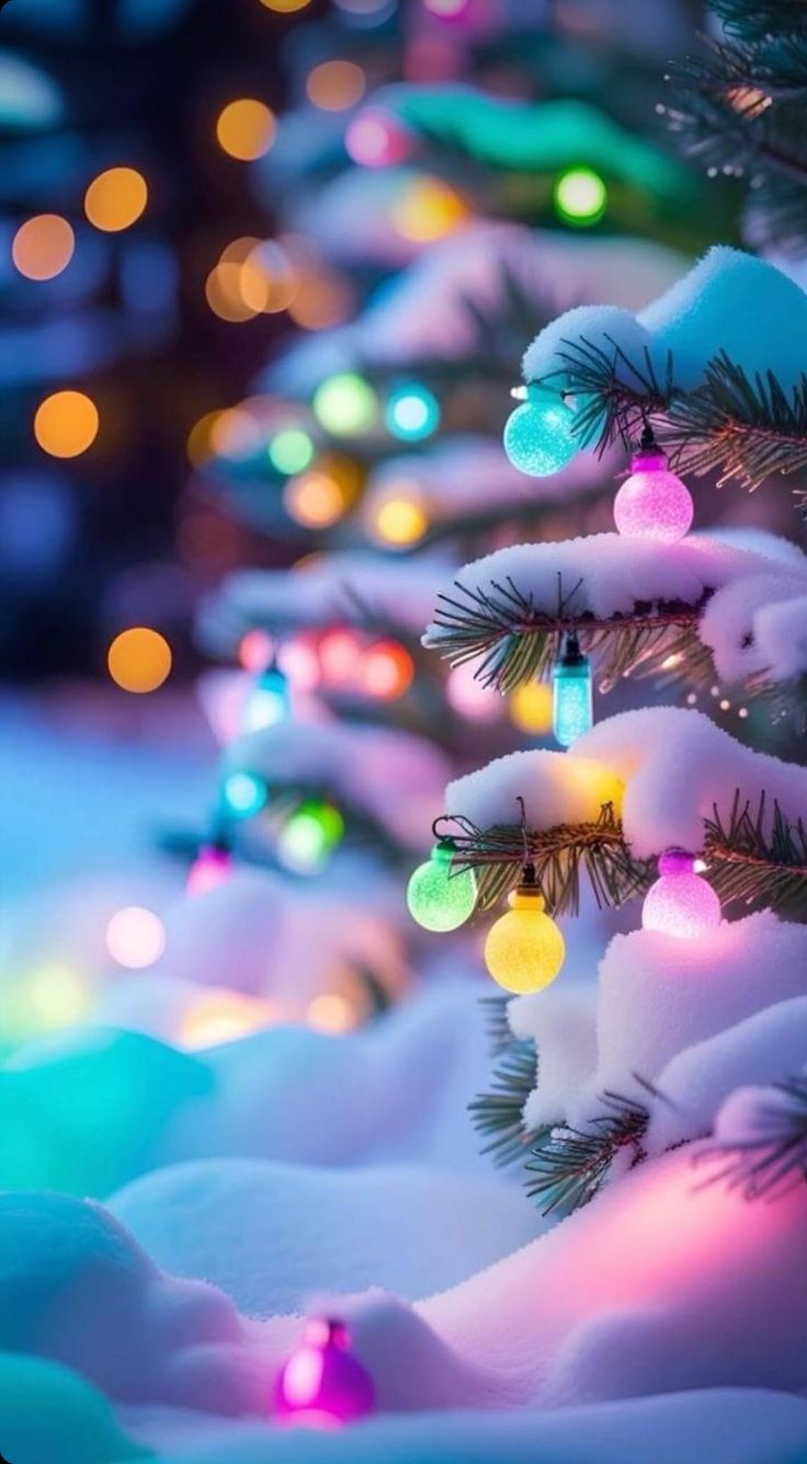 the christmas tree is decorated with colorful lights and snow covered trees are in the background