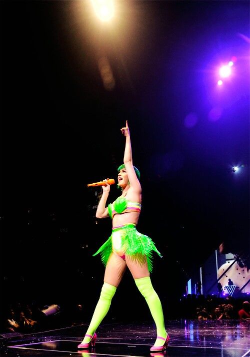 a woman in a green outfit is performing on stage with her arms up and legs crossed