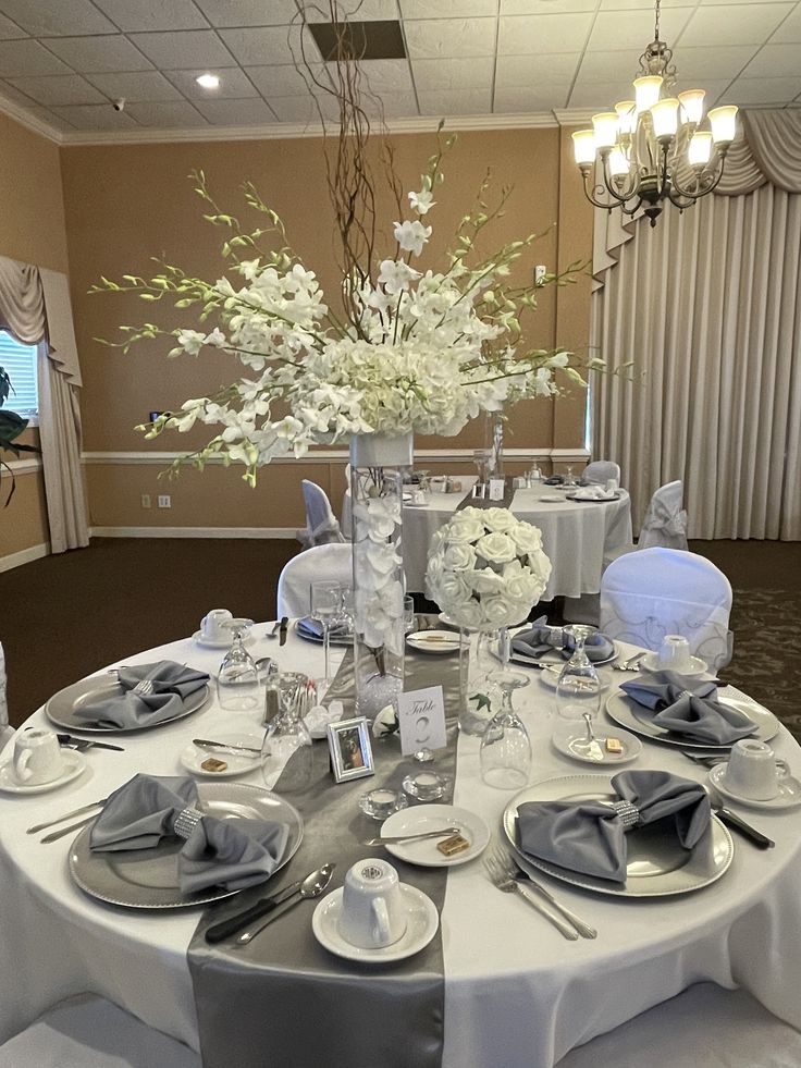 the table is set with white flowers and silverware for an elegant dinnereonal