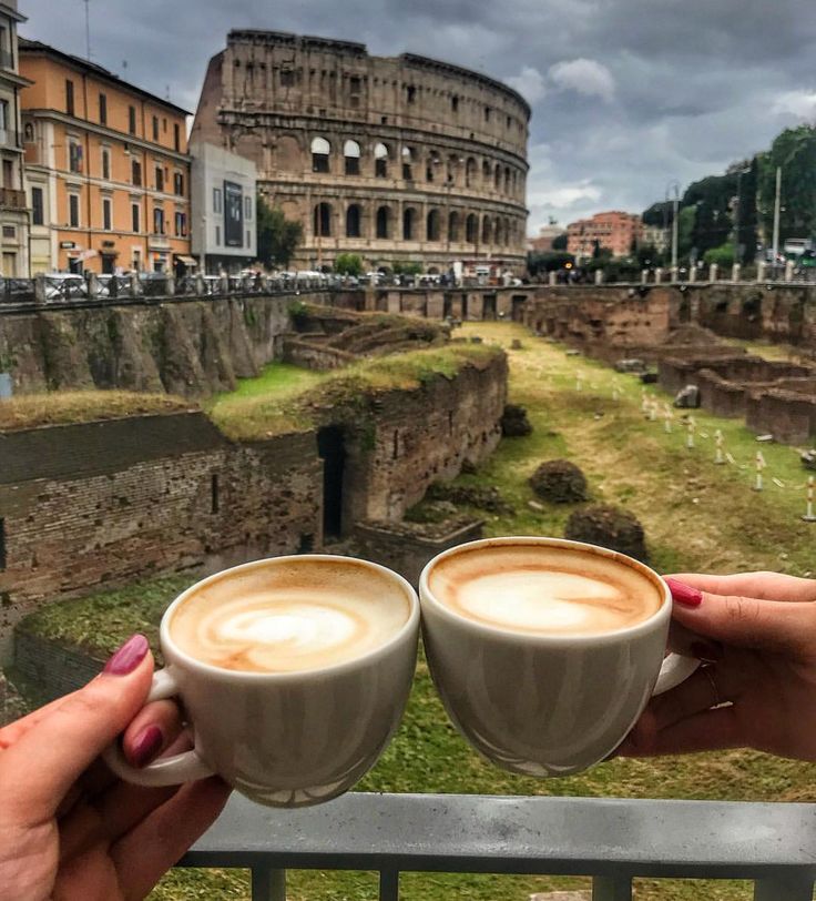 two people holding cups of coffee in front of the colossion, rome italy