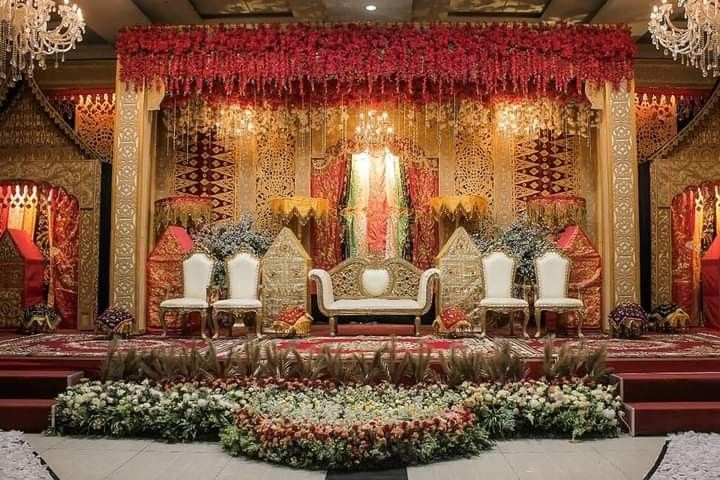 an elaborately decorated stage with white chairs and red flowers on the floor, surrounded by chandeliers