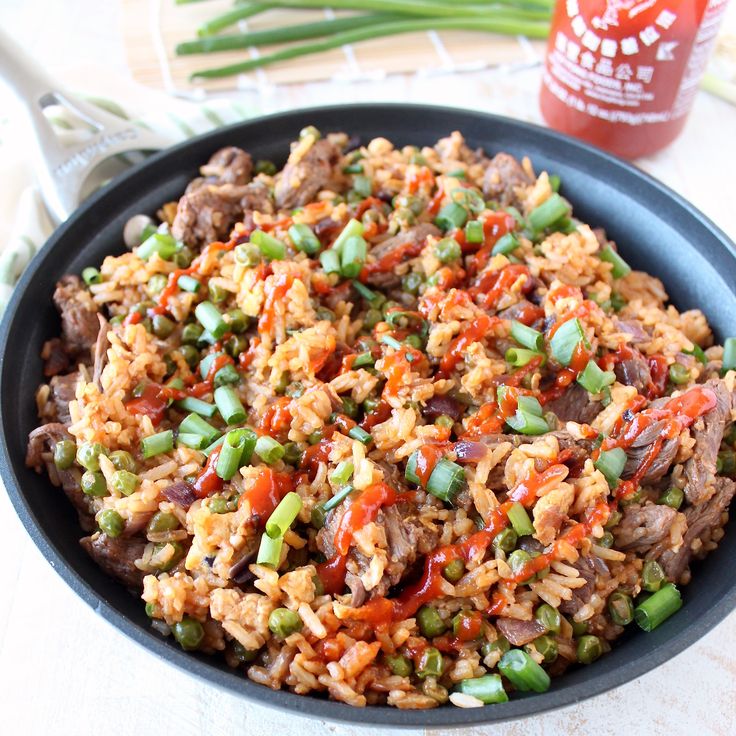 a bowl filled with rice and vegetables next to a bottle of ketchup on a table