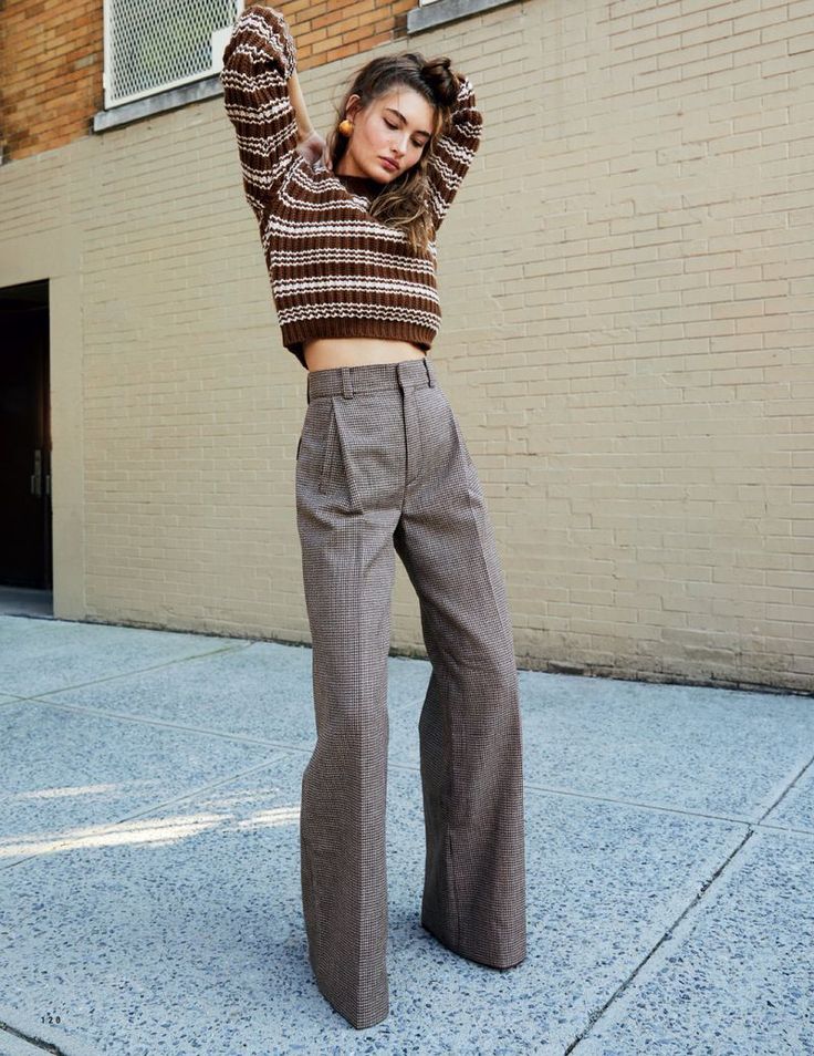 a woman standing in front of a brick building wearing high waisted pants and a cropped sweater