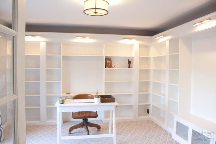 a white desk sitting in the middle of a room next to a book shelf filled with books