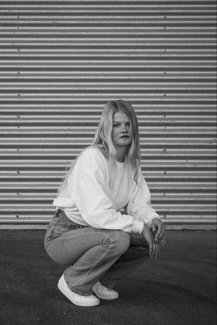 a woman squatting on the ground in front of a garage door with her hand on her knees