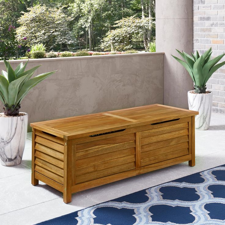 a wooden bench sitting on top of a blue rug next to two potted plants