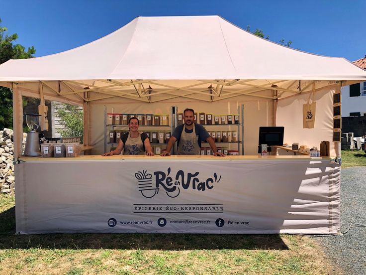 a man and woman behind a white tent with food on the table in front of it