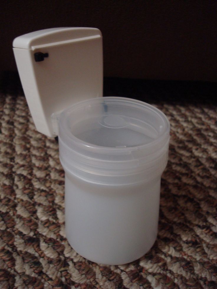 a white plastic container sitting on top of a carpeted floor next to a toilet